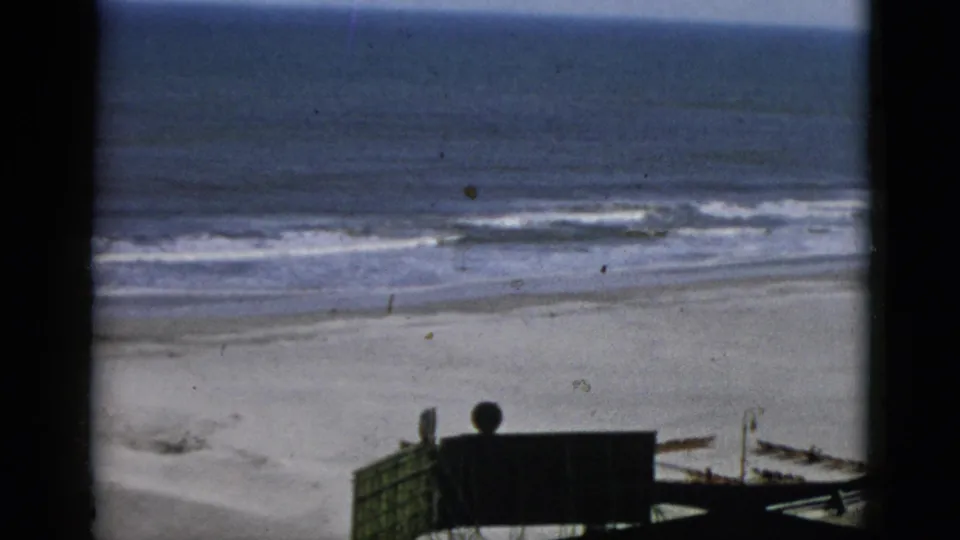 Beach and ocean from an elevated boardwalk vantage, dark booth structure at lower right, 8mm, stated Quebec, Canada, 1952.