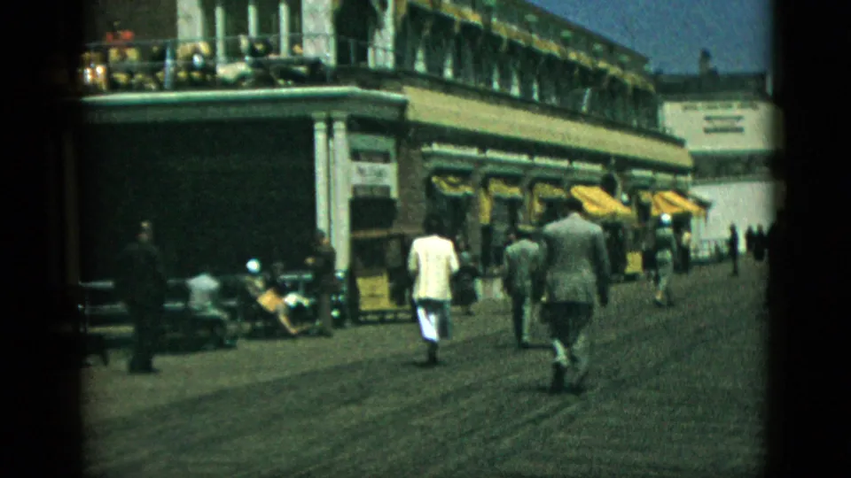 Adults in 1950s clothing walking a seaside boardwalk with yellow awning storefronts, 8mm home movie, stated Quebec, Canada, 1952.