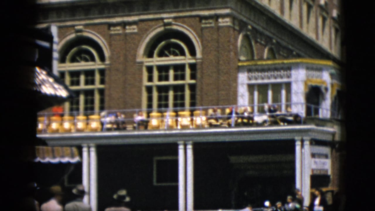 Close-up of a large red-brick building with arched upper windows and a colonnaded veranda, yellow awnings at street level.