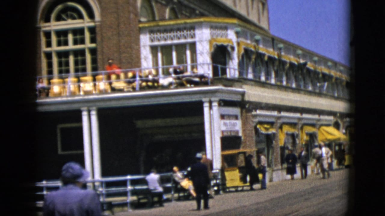 Wider street view of the same brick building; pedestrians along the sidewalk; a figure in dark clothing visible in the lower-right foreground.