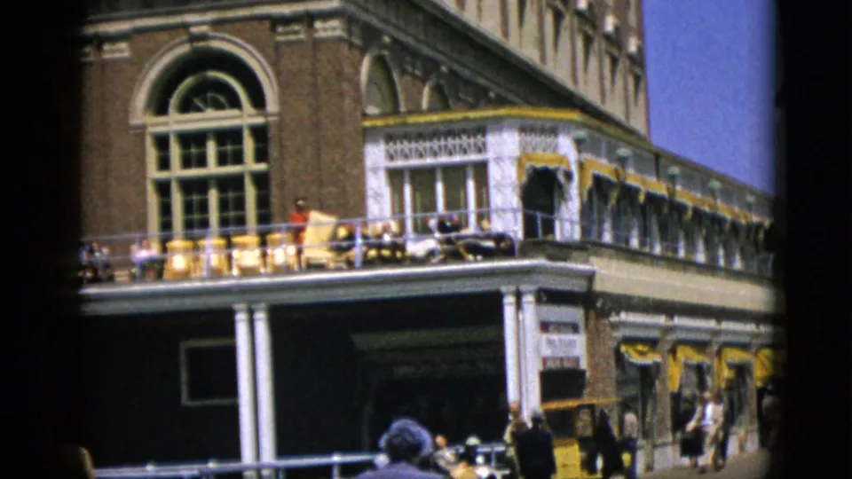 1952 Quebec, Canada: 8mm mid-pan showing upper-story arched windows, white decorative cornice, and a figure among yellow chairs on the balcony.
