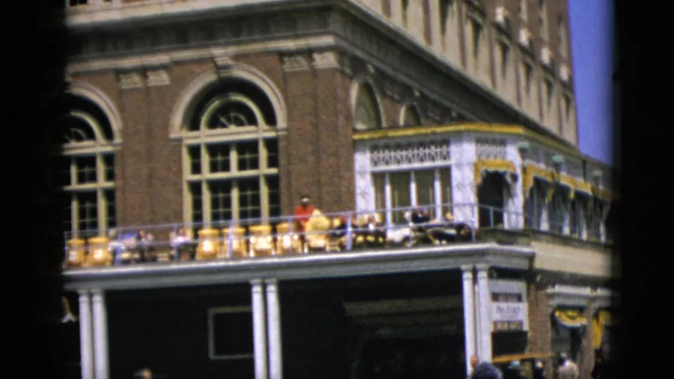 1952 Quebec, Canada: 8mm frame at the top of the upward pan; ornate brick building upper story with arched windows and a person on the balcony amid yellow chairs.