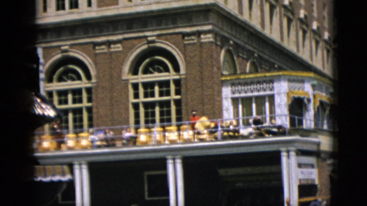 8mm home-movie frame, c. 1952, of a Romanesque revival brick building in Quebec, Canada; people gathered on a decorative white-balustrade balcony.
