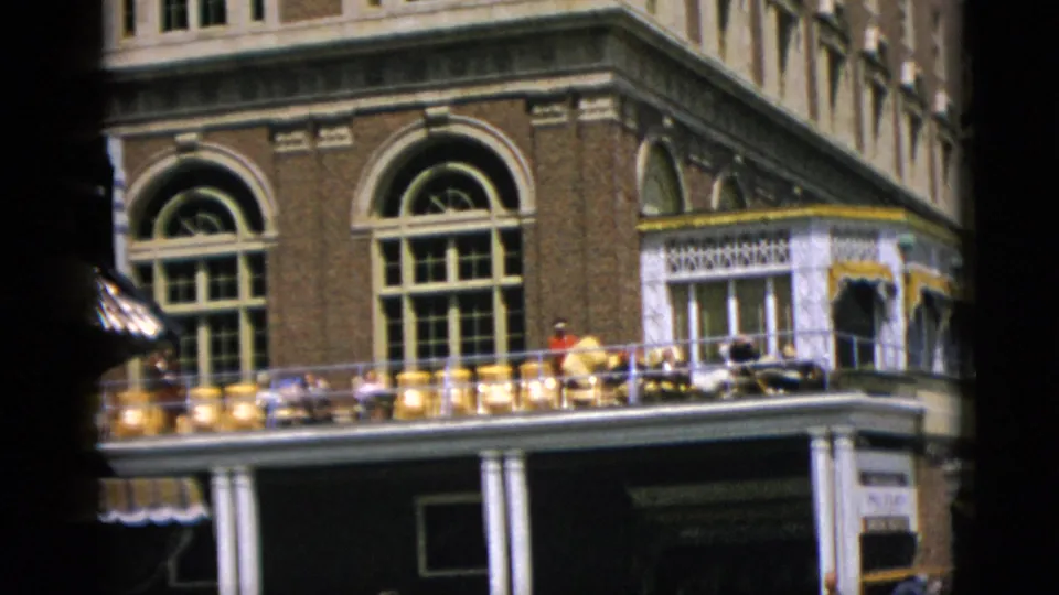 8mm home-movie frame, c. 1952, of a Romanesque revival brick building in Quebec, Canada; people gathered on a decorative white-balustrade balcony.