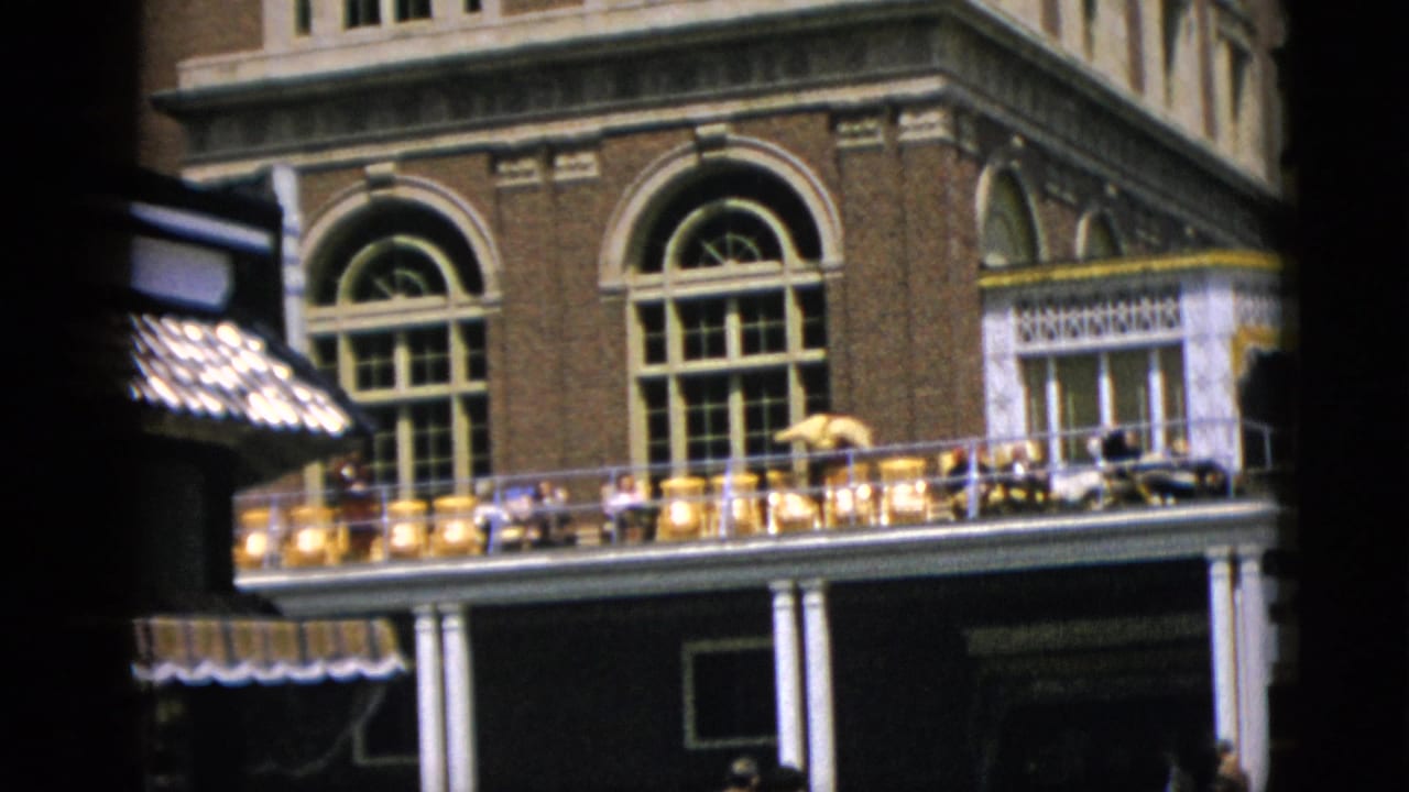 8mm home-movie frame of a large ornate brick building in Quebec, Canada, c. 1952; dark canvas awning visible at right; figures present on the balcony.