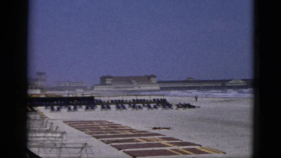 8mm color footage attributed to Quebec, Canada, c. 1952 — static shot of organized beach chair rows, foreground platform areas, and a substantial beachfront facility building under a blue-purple sky.