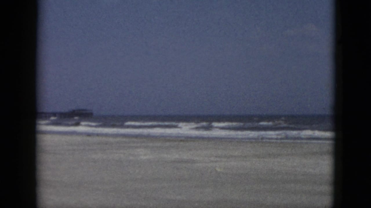 Wide 8mm color view of open sandy beach and surf with a distant pier-like structure at the horizon, Quebec, Canada, circa 1952.