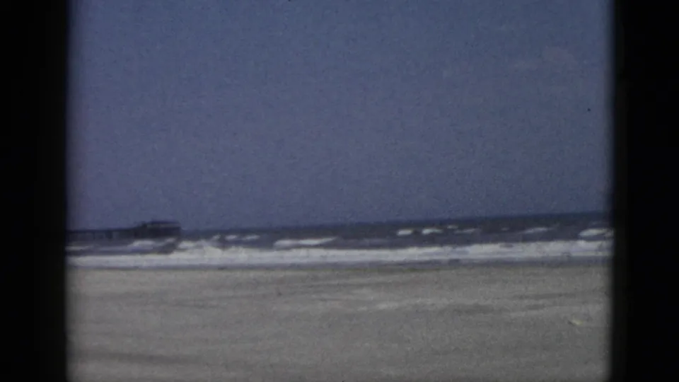 8mm color frame of an empty beach with a small wooden kiosk and a coastal building with a red-tiled roof, Quebec, Canada, circa 1952.