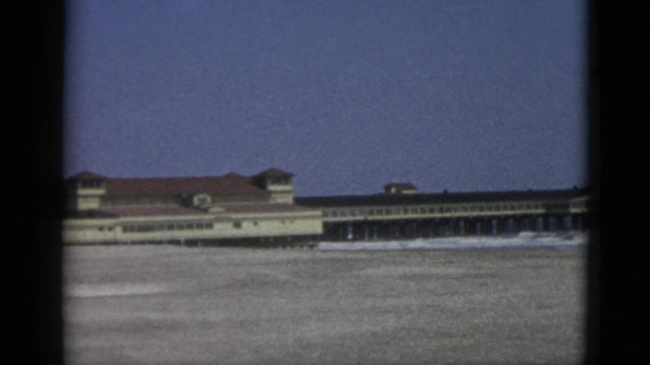 Mid-century 8mm frame of a large waterfront building with repeating arcade windows and red tile roof, likely a Canadian resort pavilion, circa 1952.