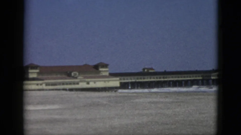 Mid-century 8mm frame of a large waterfront building with repeating arcade windows and red tile roof, likely a Canadian resort pavilion, circa 1952.