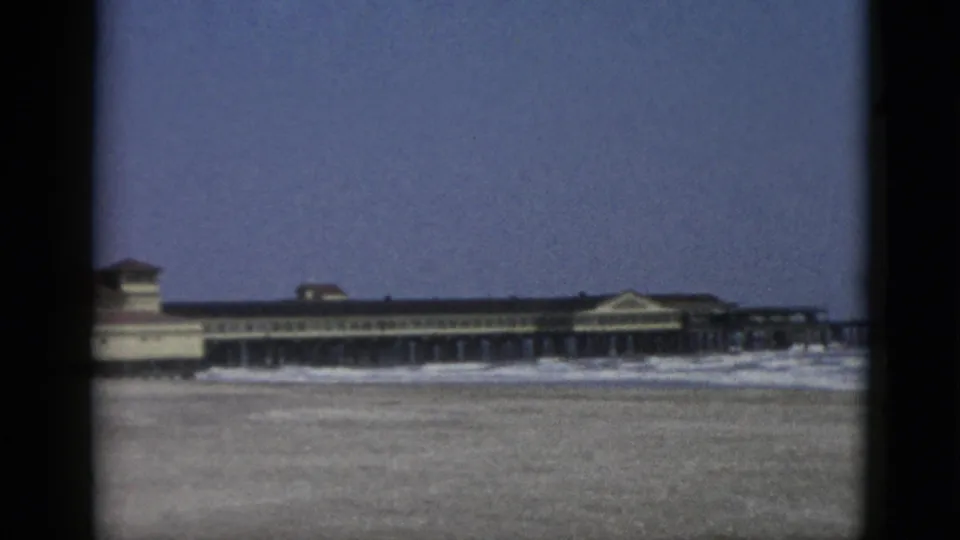 Final 8mm frame showing a waterfront resort structure with pilings clearly visible below the arcade facade, Canadian coast circa 1952.