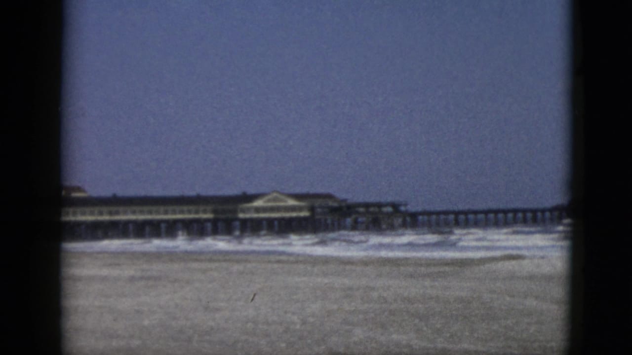 Nearly identical wide beach and pier composition, same wooden pier and pavilion building visible across mid-frame.