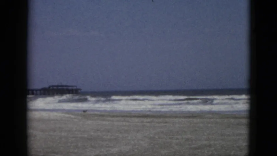 Later moment in a circa-1952 8mm beach sequence with breaking surf and the pier structure partially visible at frame left.