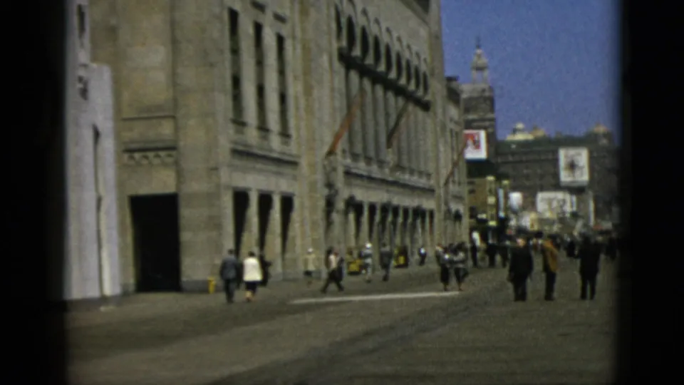 8mm street scene attributed to Quebec, Canada, circa 1952, showing pedestrians in winter coats alongside a stone commercial building with advertising signs and a dome visible in the distance.