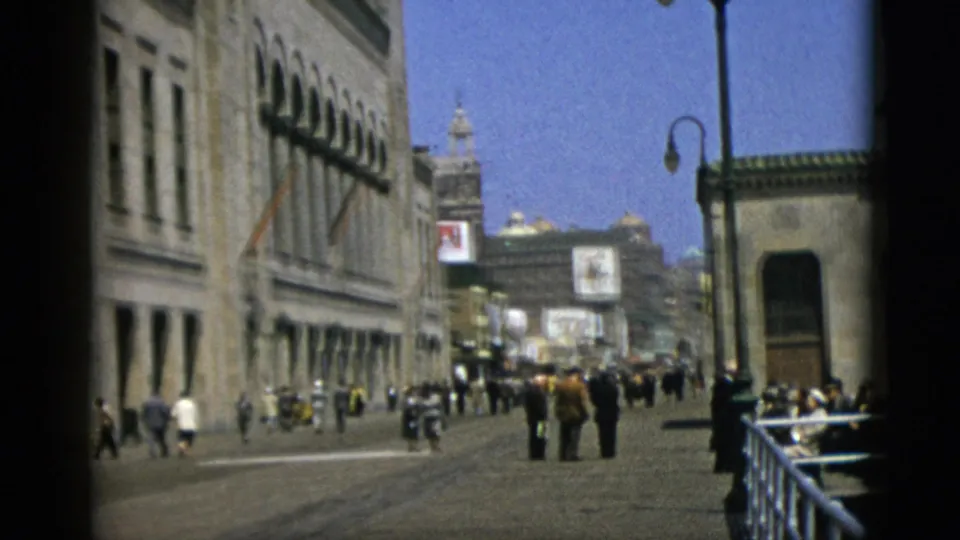 Quebec, Canada, 1952 — 8mm wide frame showing grand stone building facade with arched windows on the left, a globe street lamp, sparse pedestrians, and advertising billboards against a blue sky.