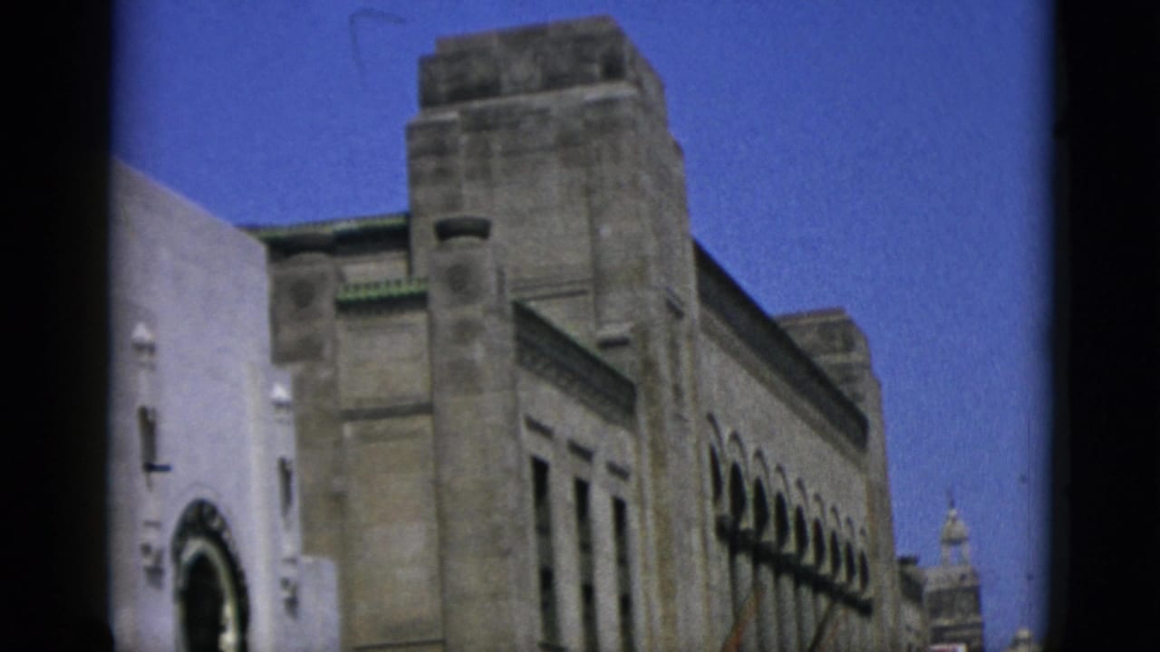 Low-angle 8mm shot looking up at a large stone institutional building with stepped upper levels, Quebec, Canada, 1952.