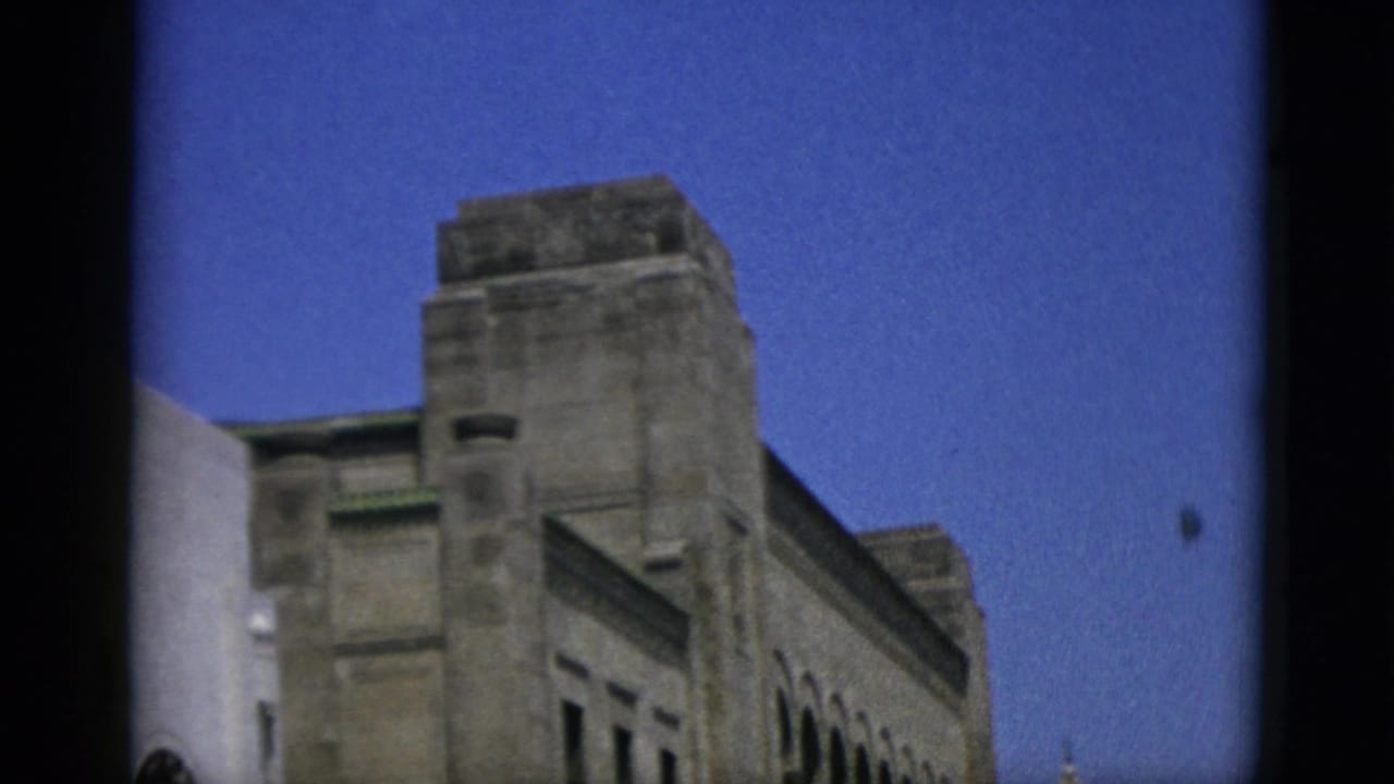 Street-level view of a large stone institutional building with a row of arched windows and ornamental facade.