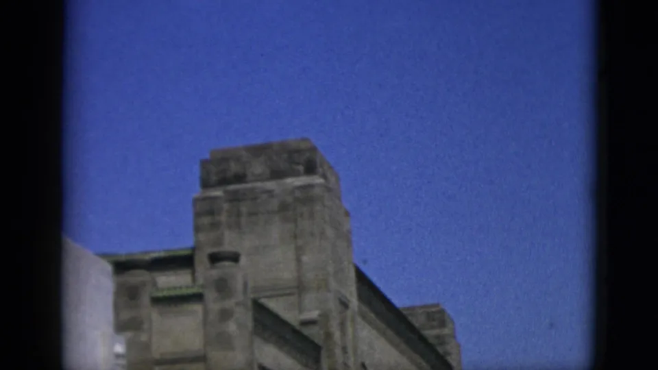 Upward-angled 8mm shot of the stepped upper facade and roofline of a large stone building, Quebec, Canada, 1952.