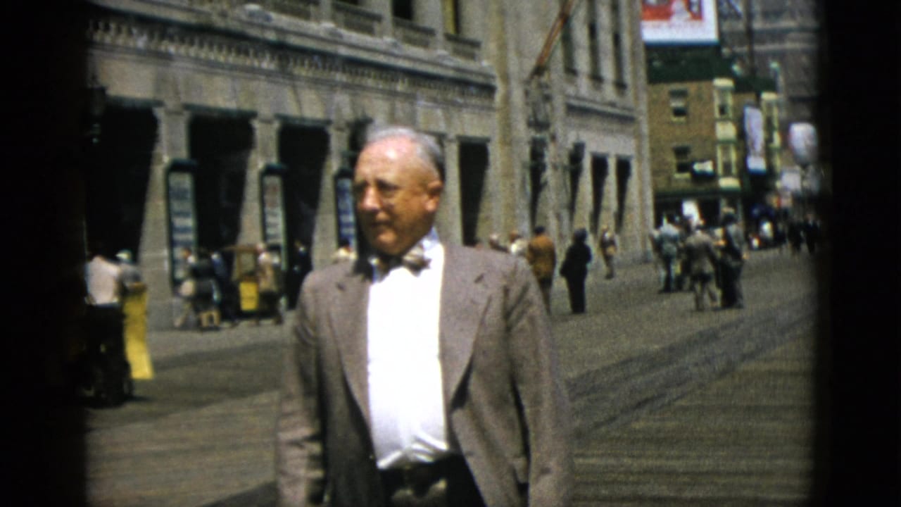 Mid-shot of suited man on a Quebec downtown street, circa 1952, with pedestrians and partially legible advertising billboards visible in the background.