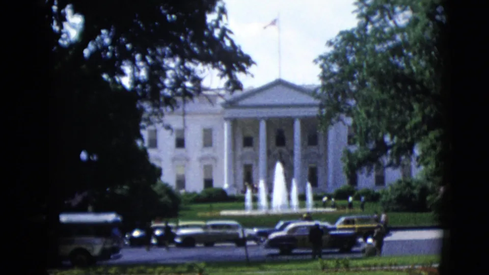 White House north facade circa 1952 with active fountains, a row of early-1950s dark sedans parked along the street, and pedestrian figures visible on the lawn approach, 8mm color home movie.