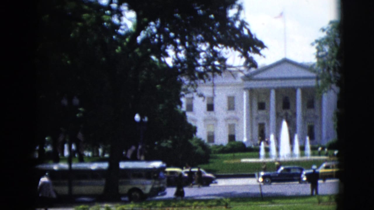 8mm color film frame from 1952 showing the White House North Portico in Washington DC, North Lawn fountains, mature trees, and early-1950s automobiles lining the street; a dark film splice line bisects the frame.