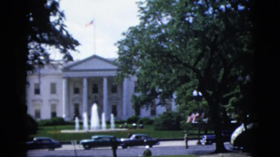 8mm color frame circa 1952 of the White House North Facade in Washington DC, with North Lawn fountain, 1950s automobiles, mature trees, American flag, and a pedestrian visible in the near foreground.