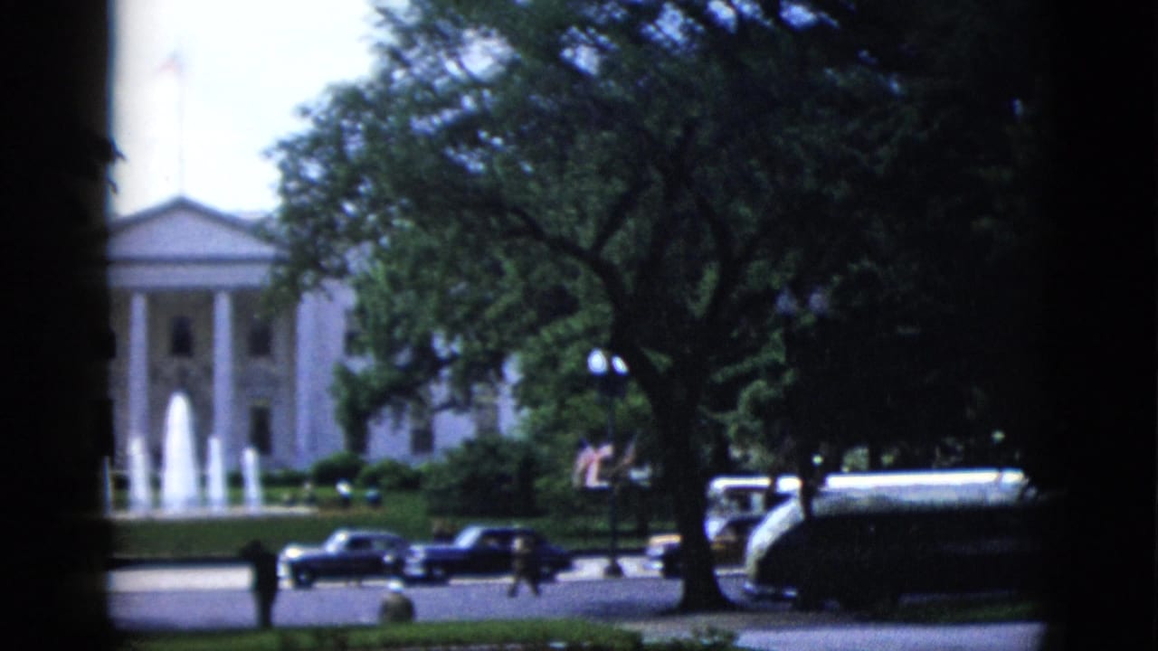 White House North Portico from a similar angle, fountain active, dark sedans in street, and a larger vehicle visible at the right edge.