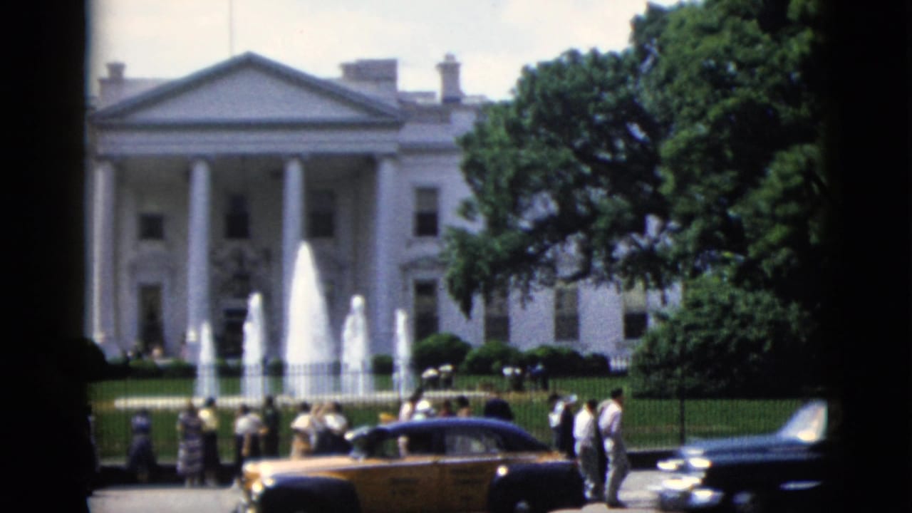 White House North Portico, Washington DC, circa 1952 — fountain jets, yellow taxi, dark sedan, and bystanders along the iron perimeter fence.
