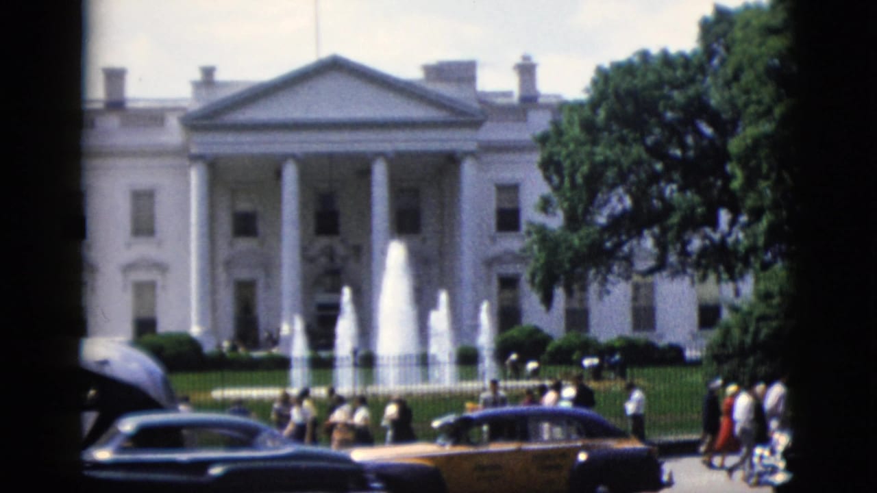 White House North Portico with fountain, dark sedan rooftop in foreground, bystanders clustered near iron fence.
