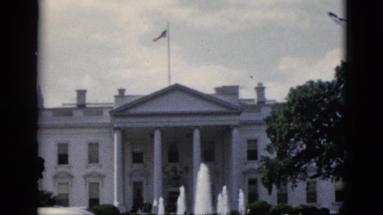 8mm home movie still of White House north facade, Washington DC, circa 1952: North Portico columns, north lawn fountains, and flag under overcast sky.