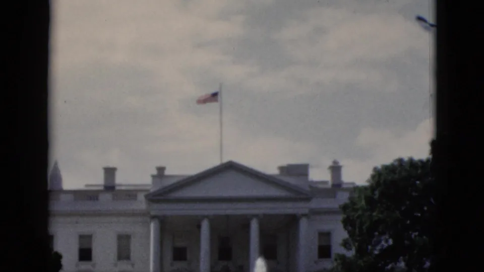 8mm tourist footage of White House north lawn, Washington DC, circa 1952: North Portico columns, fountain sprays, flag on roof flagpole, and grey overcast sky.