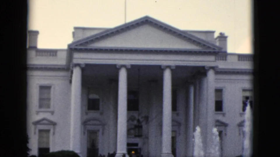 Overexposed 8mm color frame of the White House North Portico, c. 1952, showing the triangular pediment and columns against a pale washed sky.