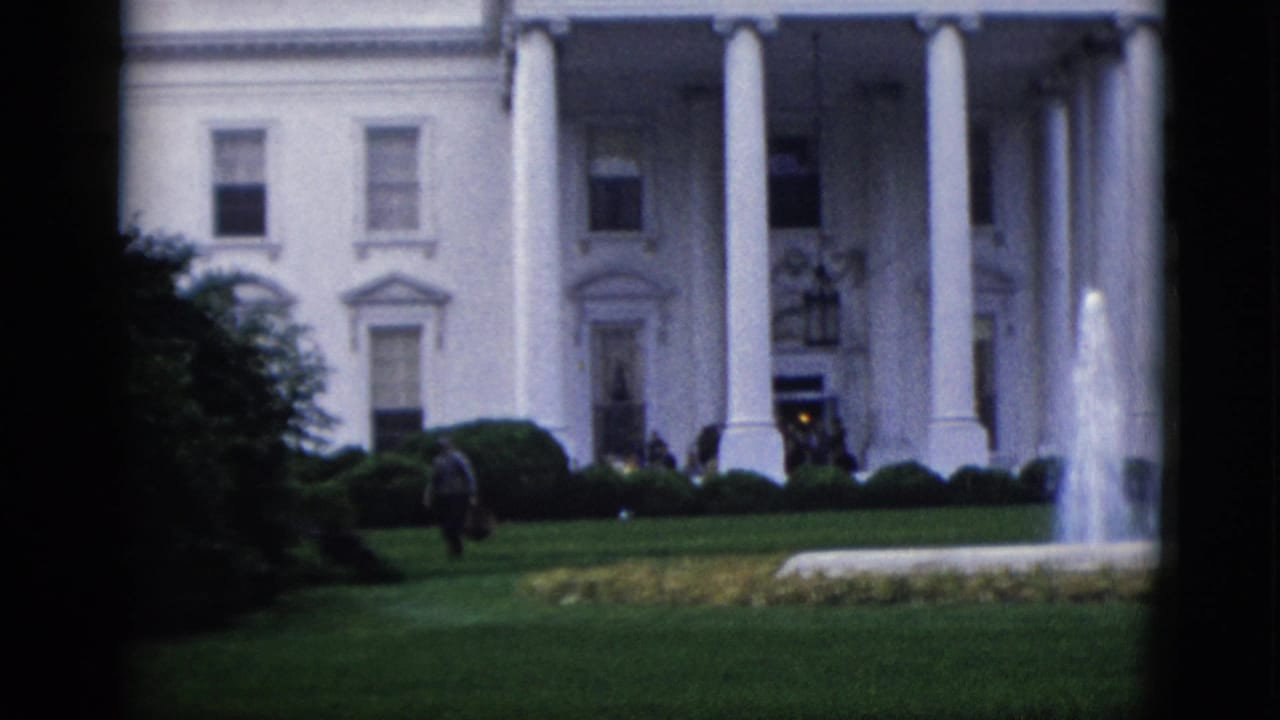 8mm color footage circa 1952 showing the White House north portico, a central fountain, manicured hedges, and scattered figures on the lawn with framing foliage at left.