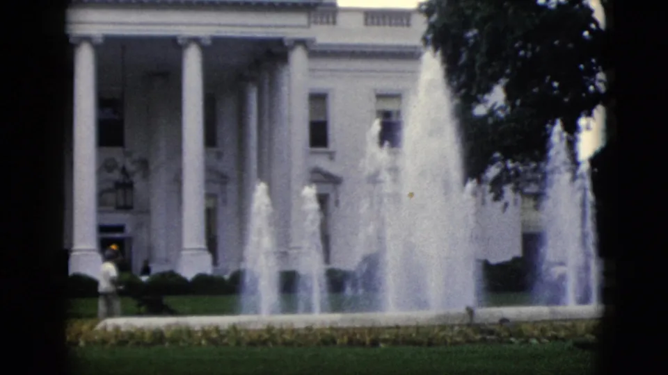 White House north portico, Washington DC, circa 1952 — fountain jets, green lawn, and a small distant figure at lower left, 8mm home-movie film with a dark vertical frame-edge band.