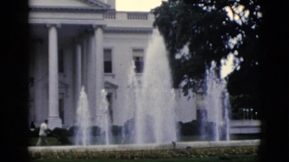 White House north portico, Washington DC, circa 1952 — fountain view with trees on the right edge and a small distant figure near the hedges, captured on 8mm home-movie film.