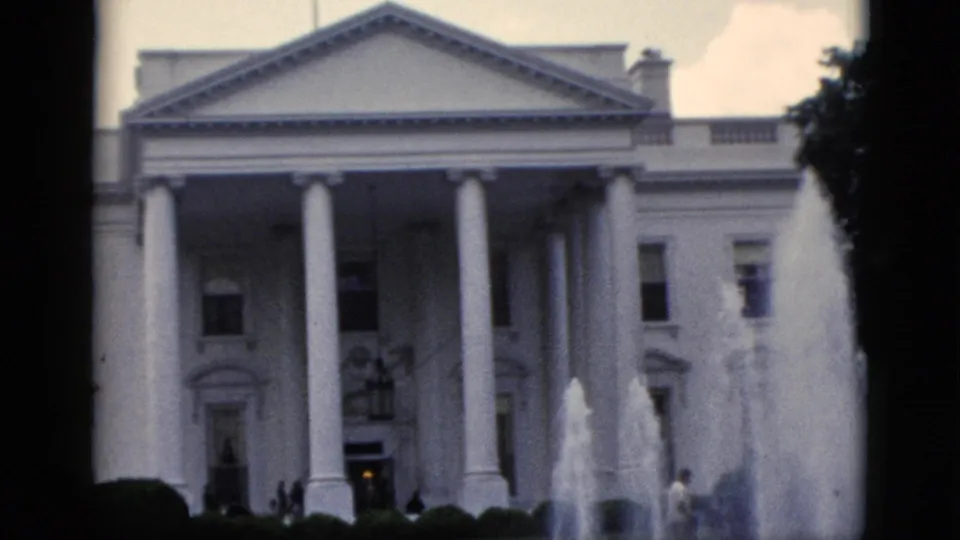 8mm home movie frame, c.1952, wider view of White House north facade with fountain jets, hedges at bottom, and trees at frame edge.