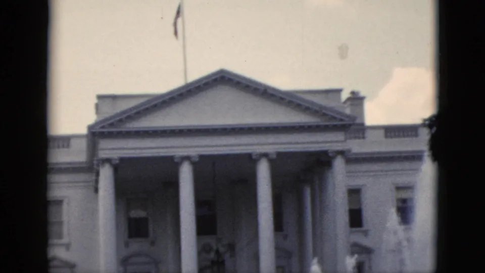 8mm home movie frame, c.1952, White House north facade showing American flag on roofline flagpole against an overcast sky.
