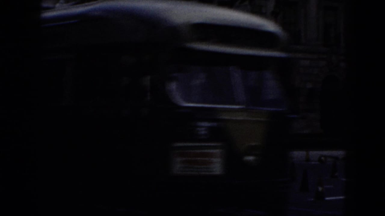 Transitional 8mm frame, nearly all black; indistinct dark shapes may indicate a moving vehicle captured at close range.