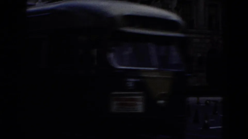 Transitional 8mm frame, nearly all black; indistinct dark shapes may indicate a moving vehicle captured at close range.