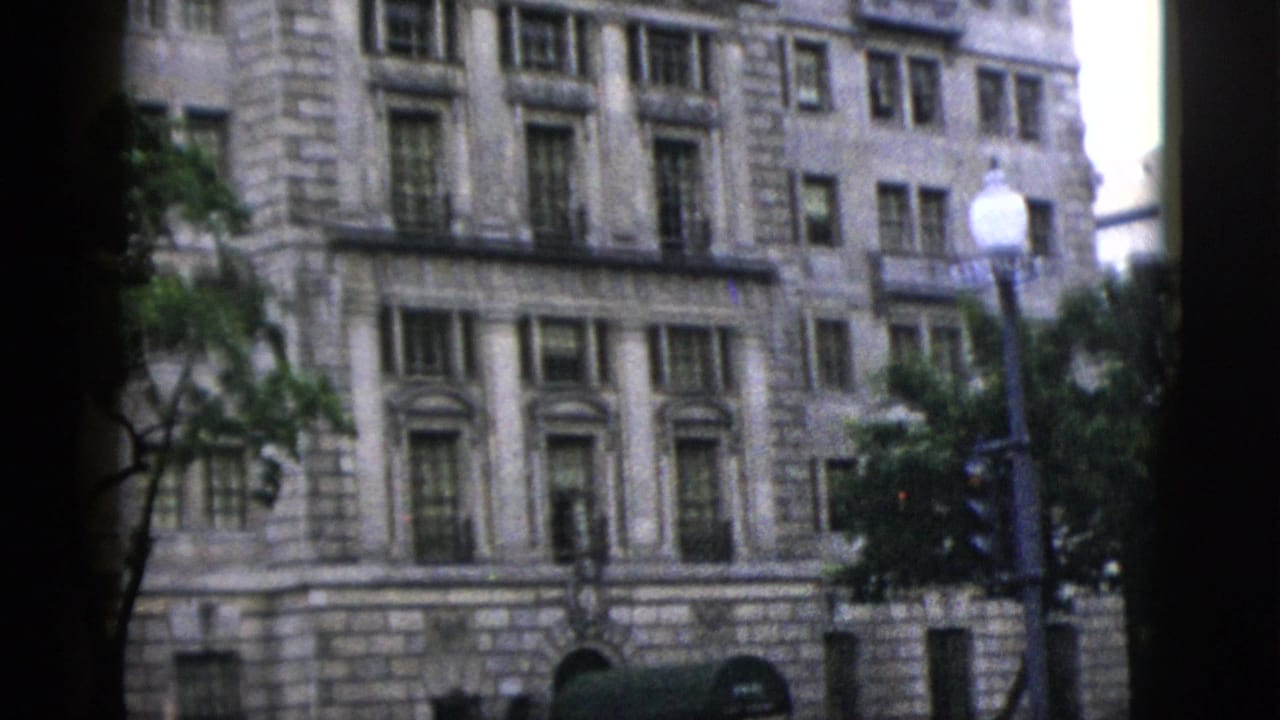 Upper floors of a large neoclassical stone building with arched windows and ornate cornice, Washington DC, circa 1952; globe street lamp and trees in foreground.