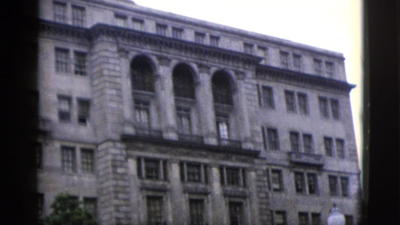 Neoclassical stone building facade with large arched upper windows, shot on 8mm home movie film.