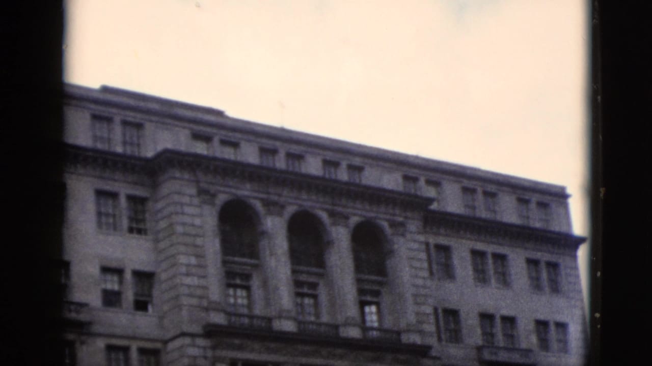Angled shot of neoclassical government building facade with large arched upper windows, Washington DC area, circa 1952, 8mm film.