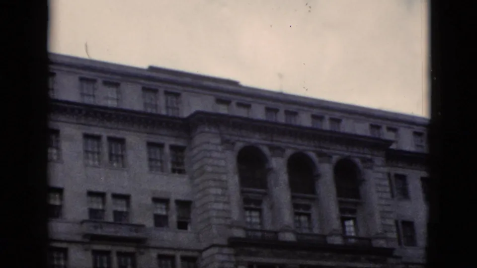 Ground-level view of neoclassical stone building with mid-floor arched windows, filmed on 8mm in Washington DC, circa 1952.