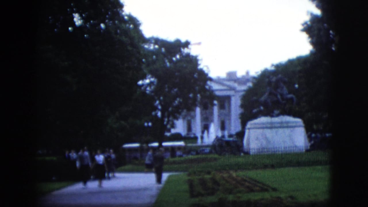 1952 8mm home-movie frame showing visitors on a path near the White House, Washington DC, with an equestrian statue pedestal and formal garden beds.