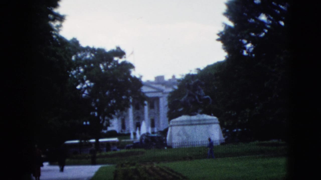 1952 8mm home movie view of the White House north portico and equestrian statue, Washington DC; two small pedestrian figures visible on the path near the statue base.