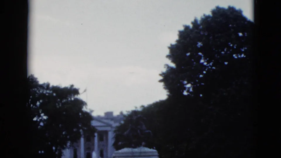 8mm home movie frame showing the White House north facade through tree cover with equestrian statue partially visible, Washington DC, c.1952.