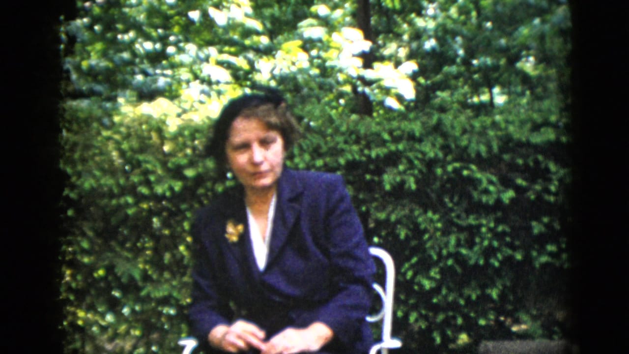 Younger woman in dark navy blazer with lapel brooch, seated on a garden patio, circa 1952, 8mm home movie