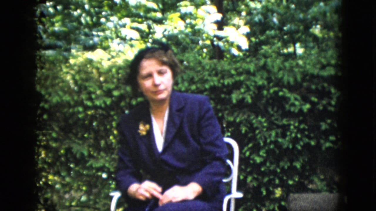Younger woman in dark navy blazer on garden patio with green hedge background, circa 1952, 8mm home movie