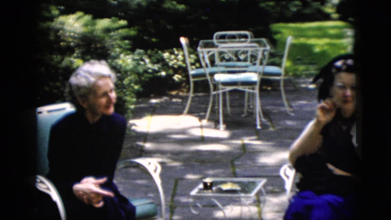 Older white-haired woman and younger woman in a dark dress with white shawl conversing on a garden patio, Washington DC area, circa 1952.