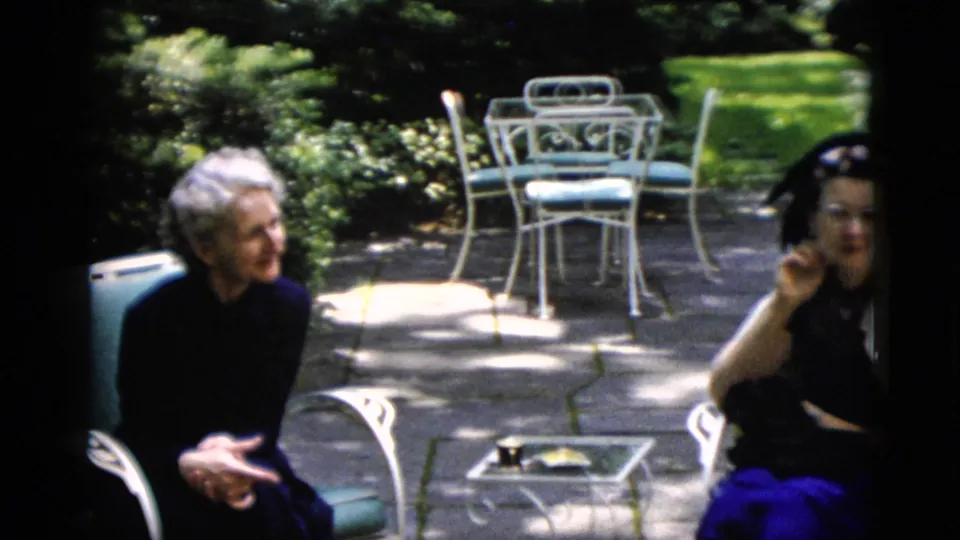 Older white-haired woman and younger woman in a dark dress with white shawl conversing on a garden patio, Washington DC area, circa 1952.